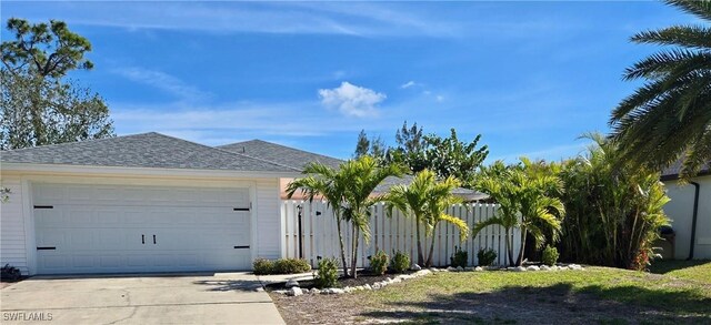 ranch-style house with concrete driveway, roof with shingles, and fence