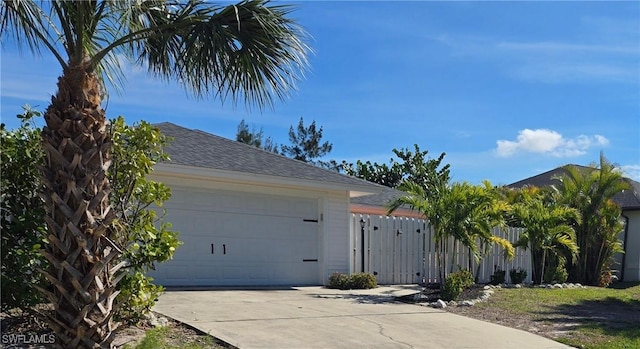 view of side of property with fence, a gate, an attached garage, a shingled roof, and driveway