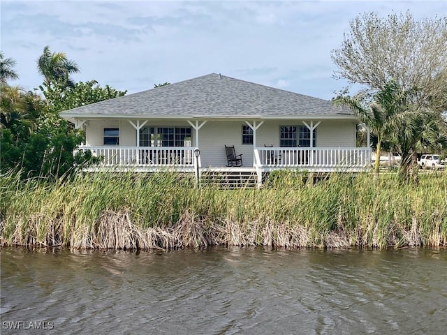 rear view of house with a water view, a porch, and a shingled roof