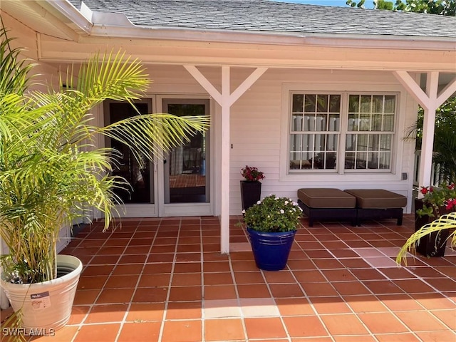 view of exterior entry featuring a patio and a shingled roof