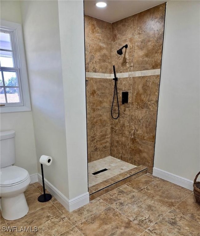 bathroom with baseboards, toilet, and a tile shower