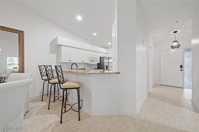 kitchen with white appliances, light stone countertops, light tile patterned flooring, white cabinets, and a kitchen bar