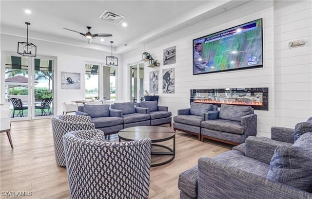 living area featuring a ceiling fan, visible vents, light wood-style flooring, recessed lighting, and a glass covered fireplace