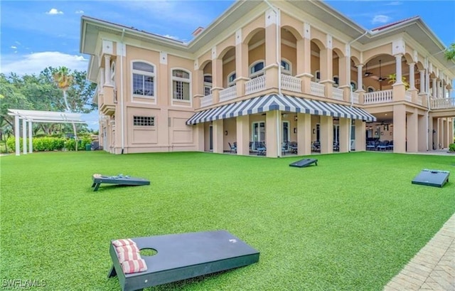 back of property with ceiling fan, a balcony, a lawn, and stucco siding