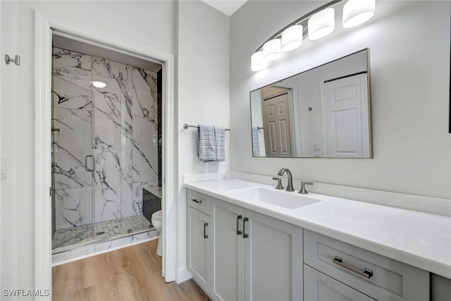 bathroom featuring a marble finish shower, toilet, wood finished floors, and vanity