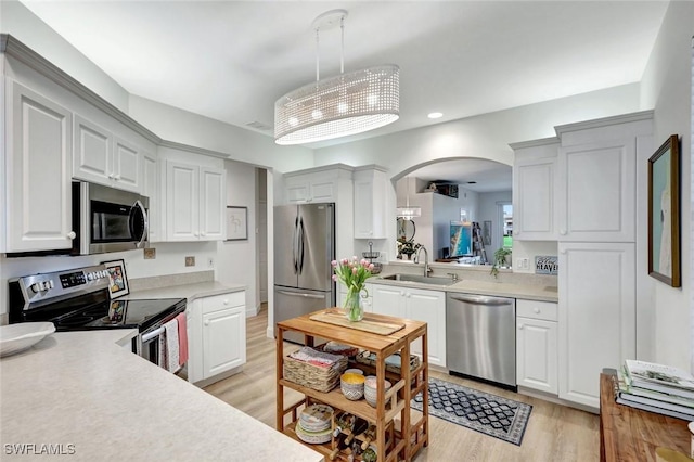 kitchen featuring light wood-style flooring, arched walkways, a sink, light countertops, and appliances with stainless steel finishes