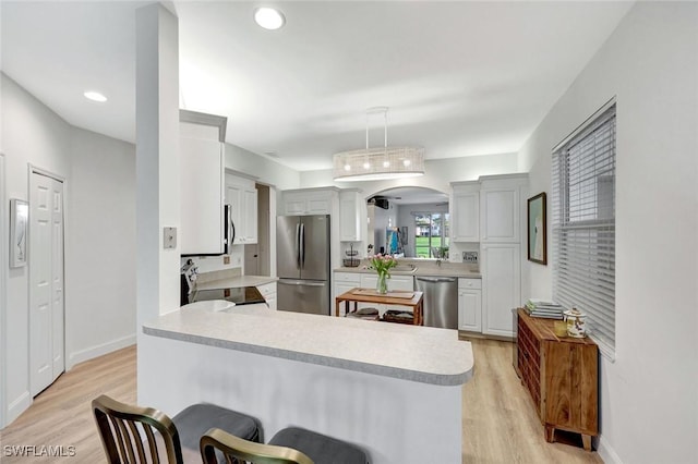 kitchen featuring a kitchen bar, light wood-style flooring, stainless steel appliances, arched walkways, and light countertops