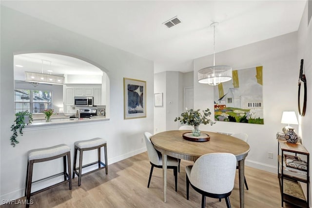 dining area with baseboards, arched walkways, visible vents, and light wood finished floors