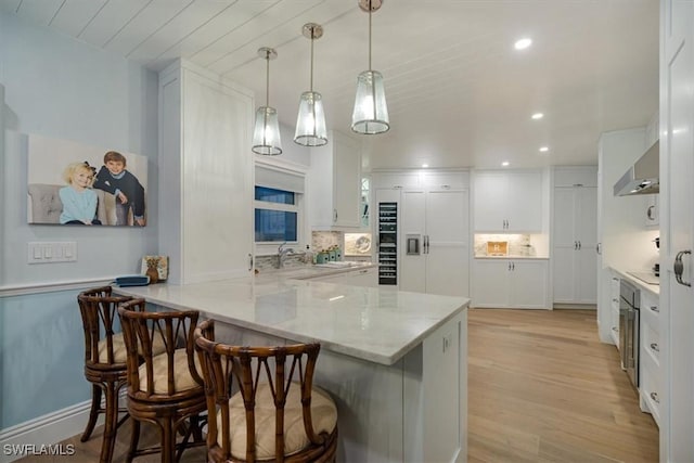 kitchen with a peninsula, a kitchen breakfast bar, white cabinets, wall chimney range hood, and backsplash