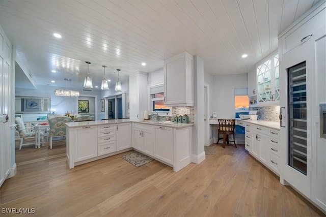 kitchen with light wood finished floors, backsplash, a peninsula, white cabinets, and light countertops