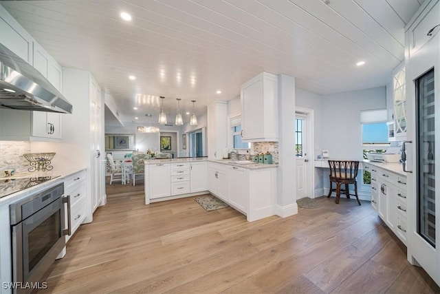 kitchen with light wood-type flooring, stainless steel microwave, ventilation hood, a peninsula, and decorative backsplash