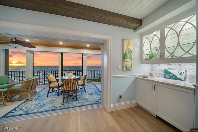 dining area with ceiling fan, a water view, beamed ceiling, light wood-style flooring, and wooden ceiling