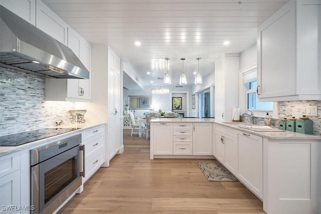 kitchen featuring oven, under cabinet range hood, a peninsula, white cabinets, and black electric stovetop