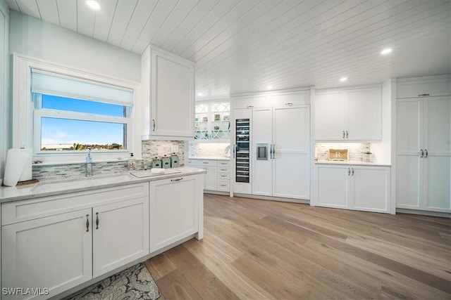 kitchen with paneled fridge, a sink, decorative backsplash, white cabinets, and light wood-style floors