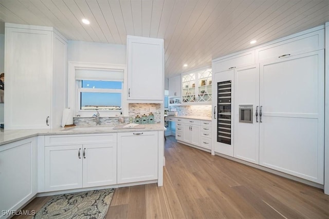 kitchen with a sink, white cabinets, wood ceiling, light wood-type flooring, and backsplash