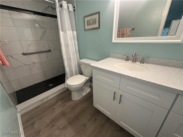 bathroom with toilet, wood finished floors, vanity, and a tile shower