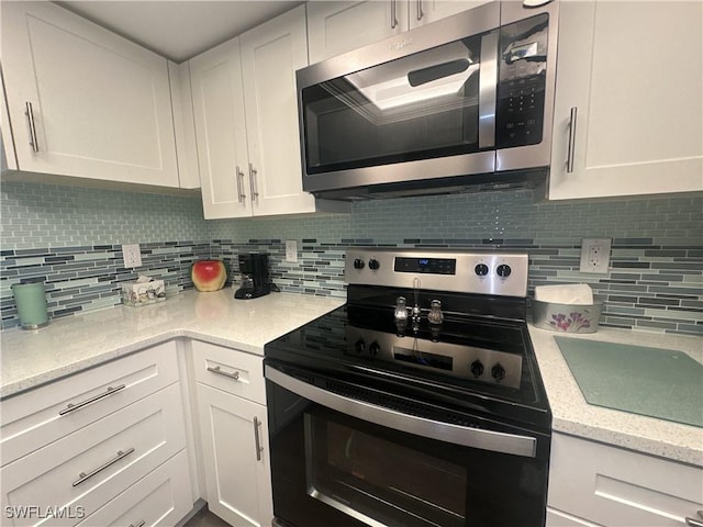 kitchen featuring light stone countertops, decorative backsplash, white cabinets, stainless steel microwave, and black electric range oven