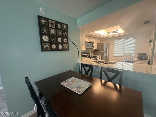 dining area featuring visible vents, a raised ceiling, baseboards, and ceiling fan