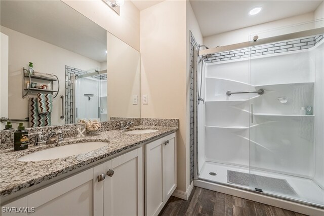 bathroom featuring double vanity, a stall shower, wood finished floors, and a sink