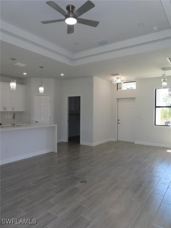 unfurnished living room with wood finish floors, baseboards, a raised ceiling, and ceiling fan