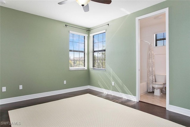 unfurnished bedroom featuring connected bathroom, baseboards, dark wood finished floors, and a ceiling fan