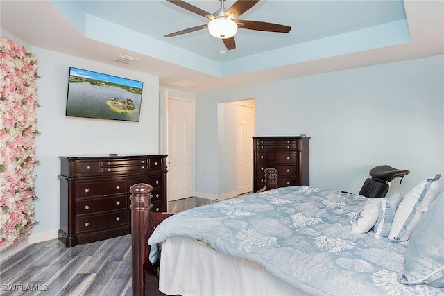 bedroom with a tray ceiling, visible vents, dark wood-type flooring, and baseboards