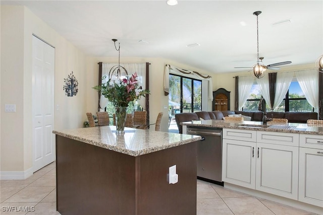 kitchen featuring light tile patterned floors, a kitchen island, stainless steel dishwasher, and light stone counters