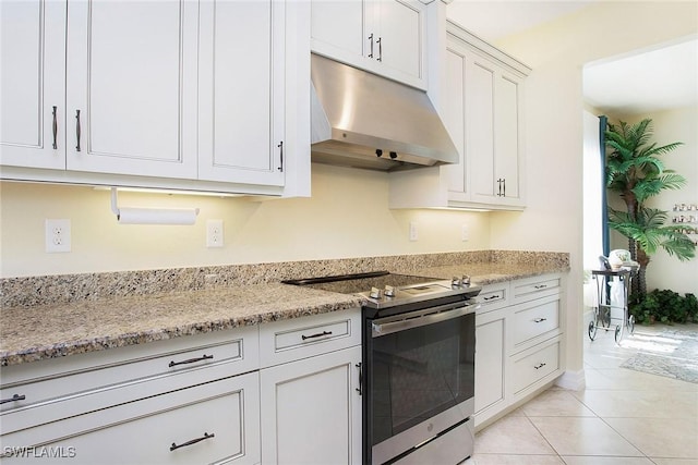 kitchen with under cabinet range hood, stainless steel electric stove, white cabinets, and light tile patterned floors