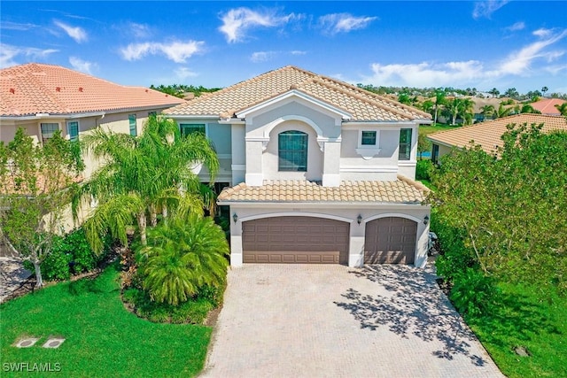 mediterranean / spanish home with a tile roof, decorative driveway, a garage, and stucco siding