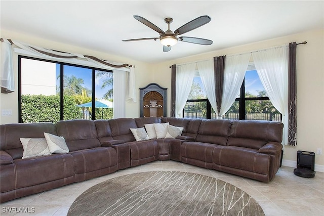 tiled living area featuring baseboards, a healthy amount of sunlight, and a ceiling fan