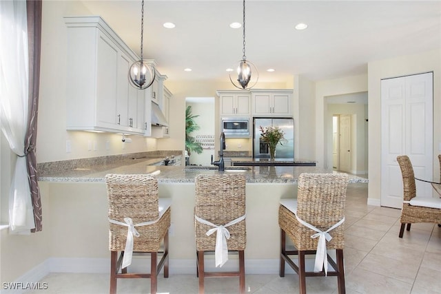 kitchen featuring a peninsula, a sink, stainless steel appliances, under cabinet range hood, and a kitchen bar