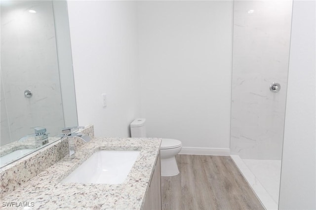 bathroom featuring vanity, wood finished floors, baseboards, walk in shower, and toilet