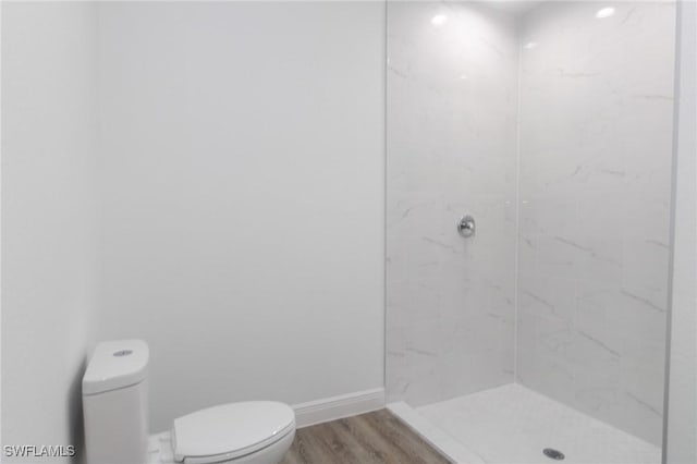 bathroom featuring toilet, wood finished floors, baseboards, and walk in shower