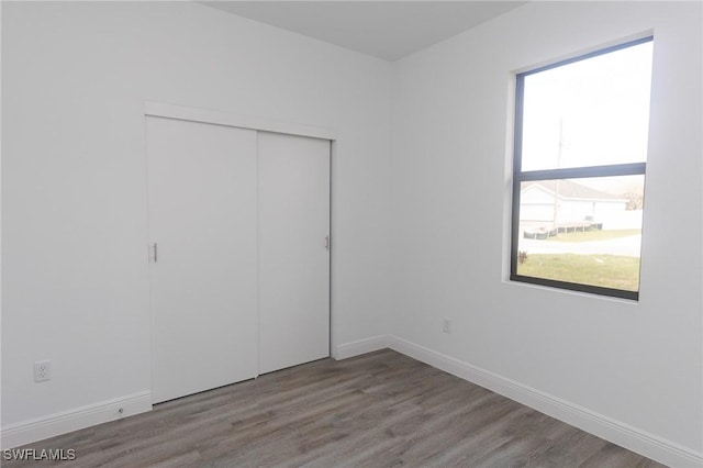 unfurnished bedroom featuring wood finished floors, a closet, and baseboards