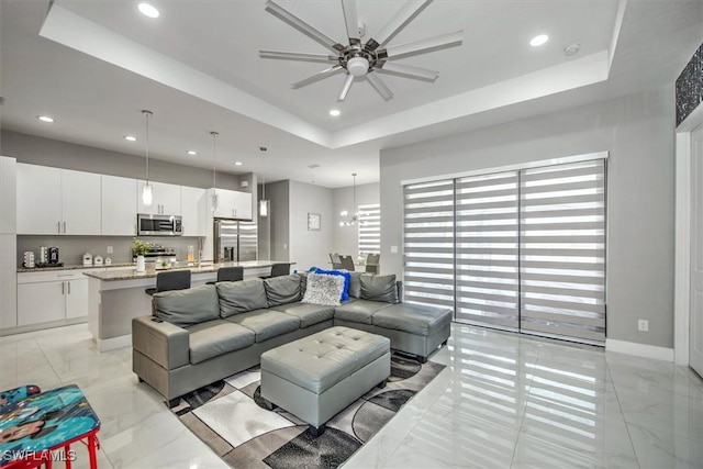 living room featuring a tray ceiling, recessed lighting, marble finish floor, and baseboards