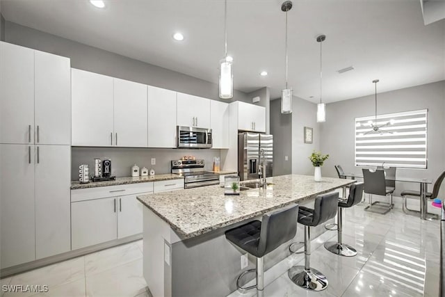 kitchen featuring a breakfast bar, an island with sink, white cabinets, appliances with stainless steel finishes, and marble finish floor