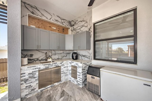 kitchen with marble finish floor, gray cabinetry, a sink, refrigerator, and light countertops