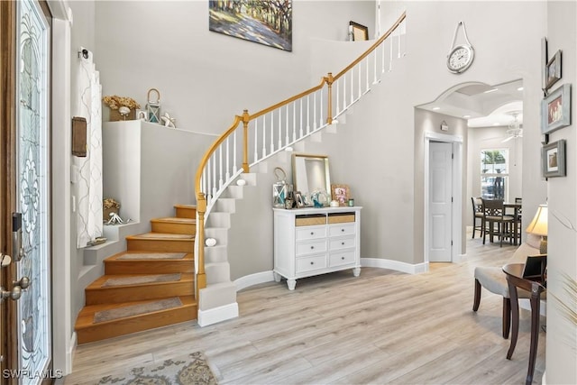 foyer with wood finished floors, baseboards, a high ceiling, arched walkways, and stairs