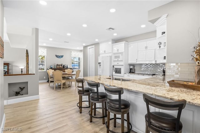 kitchen featuring a sink, white cabinetry, white appliances, a peninsula, and light stone countertops