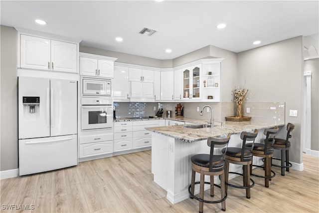 kitchen featuring visible vents, light stone counters, a peninsula, white appliances, and a sink