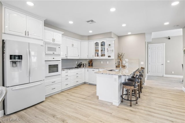 kitchen with white appliances, visible vents, a peninsula, a sink, and white cabinetry