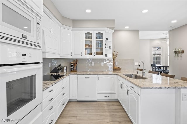 kitchen with white appliances, a peninsula, a sink, decorative backsplash, and white cabinetry