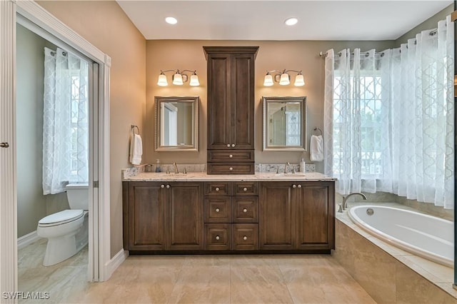 bathroom featuring a sink, plenty of natural light, a garden tub, and toilet