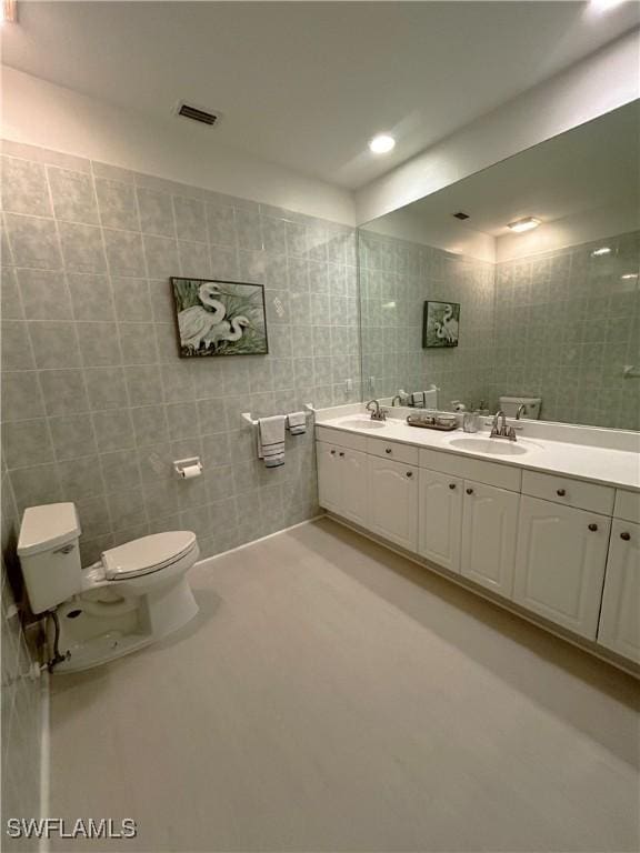 full bathroom with a sink, toilet, tile walls, and double vanity