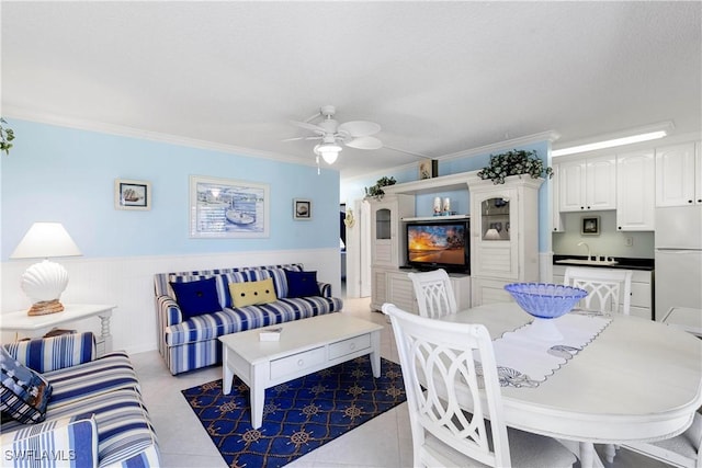 tiled living room featuring ceiling fan, ornamental molding, a wainscoted wall, and a sink