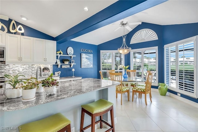 kitchen featuring light stone countertops, a kitchen bar, lofted ceiling with beams, white cabinetry, and open shelves