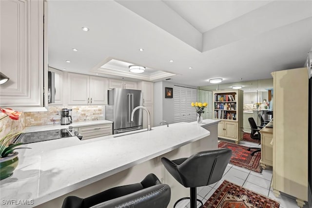 kitchen featuring a tray ceiling, a peninsula, decorative backsplash, a kitchen breakfast bar, and high quality fridge