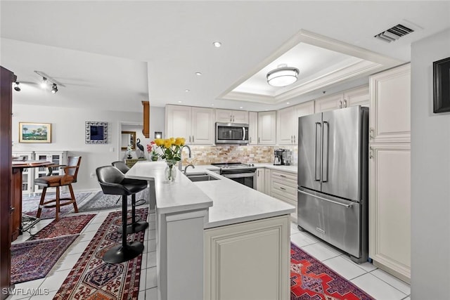 kitchen with visible vents, a sink, a tray ceiling, stainless steel appliances, and light tile patterned floors