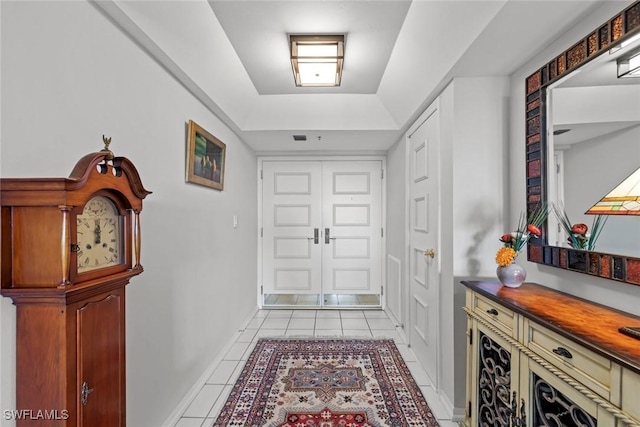 foyer entrance featuring a raised ceiling, light tile patterned flooring, and baseboards