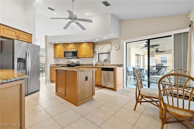 kitchen with visible vents, a ceiling fan, light stone counters, a kitchen island, and appliances with stainless steel finishes